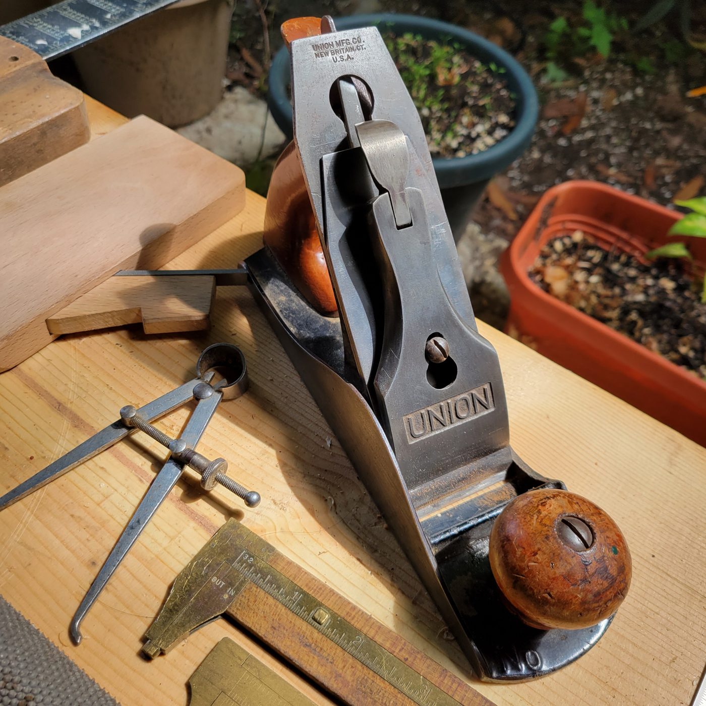A vintage Union hand plane on Terry's bench, with brass calipers and dividers beside a board cut for a joint.